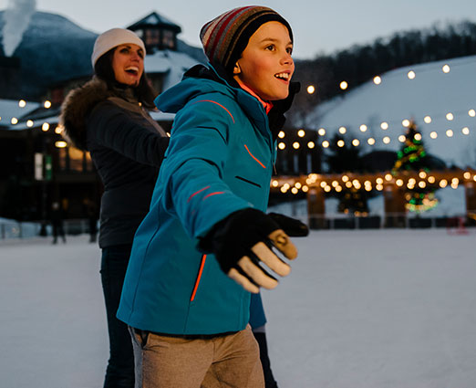 A mother and her sun ice skating in the evening - The Lodge at Spruce Peak