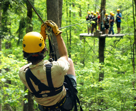 figure of a man on a zipline through lush forested trees